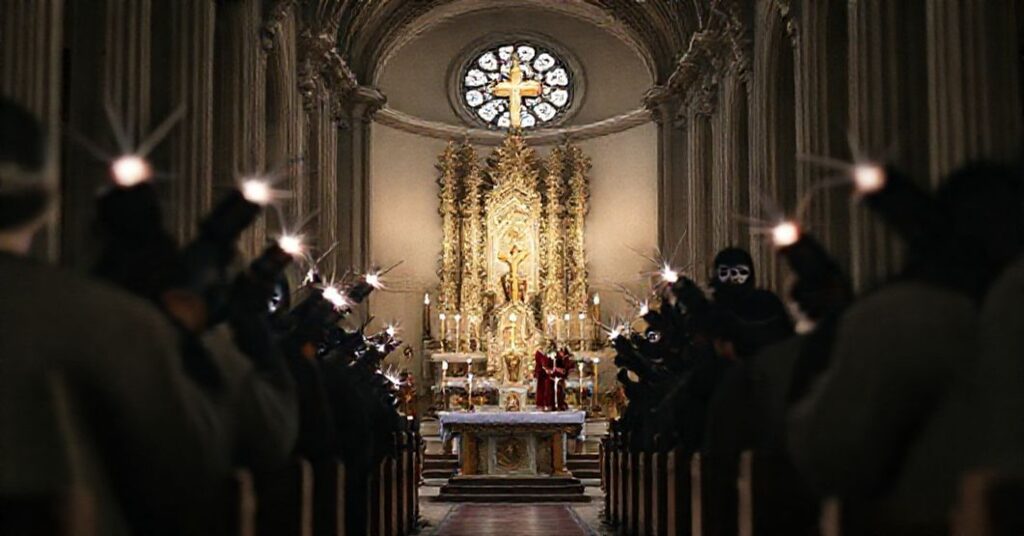 Wnętrze wiedeńskiej Karlskirche podczas tradycyjnej mszy katolickiej z tabernakulum i ołtarzem na pierwszym planie. Na tle widoczne są rozmyte postacie w demonicznych kostiumach i maskach trzymające fałszywe bomby z migającymi światłami.