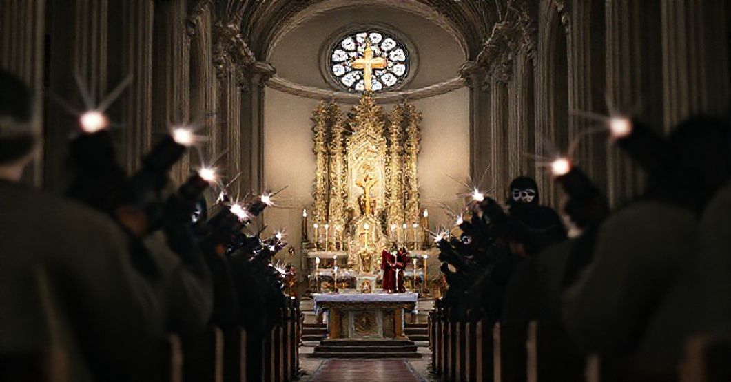 Fałszywa bomba w wiedeńskiej świątyni - atak na życie i wiarę Wnętrze wiedeńskiej Karlskirche podczas tradycyjnej mszy katolickiej z tabernakulum i ołtarzem na pierwszym planie. Na tle widoczne są rozmyte postacie w demonicznych kostiumach i maskach trzymające fałszywe bomby z migającymi światłami.