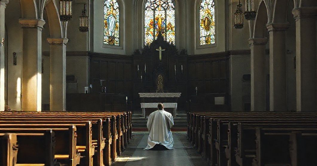 Wewnątrz porzuconego kościoła katolickiego z pustym ołtarzem i o samotnym kapłanie modlącego się na kolanach wśród pustych ławek.