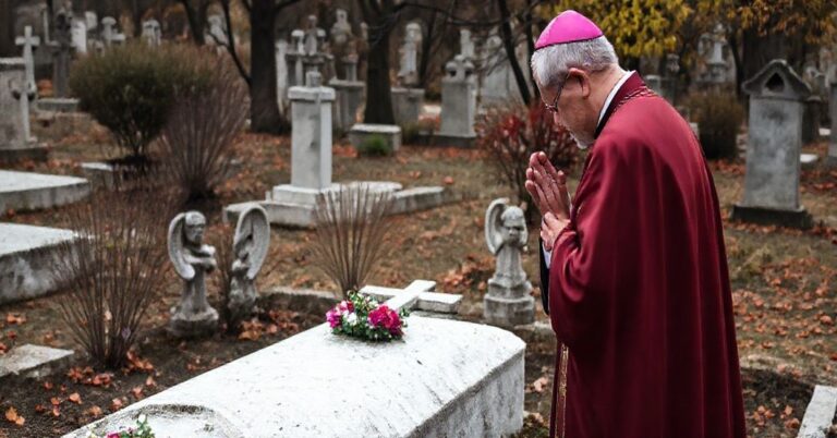 Ceremonia religijna przy Grobie Dzieci Utraconych w Łomży, z biskupem w szatach liturgicznych modlącym się przy skromnym grobie z krzyżem i aniołami z kamienia.