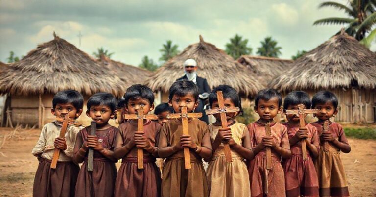 Grupa dzieci w tradycyjnych ubraniach przed wioską w Sri Lance trzymających drewniane krzyże, symbolizujących misyjne zadanie Kościoła z perspektywy katolickiej tradycji.
