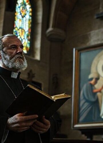 Ks. Nikos Skuras w tradycyjnym kościele katolickim obok kontrowersyjnego malowidła modernistycznego.