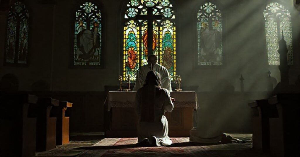 Juman Al Qawasmi klęcząca przed tradycyjnym katolickim ołtarzem z księdzem w sutannie i stole przyjmującym jej Eucharystię; w tle widoczne kontury meczetu.