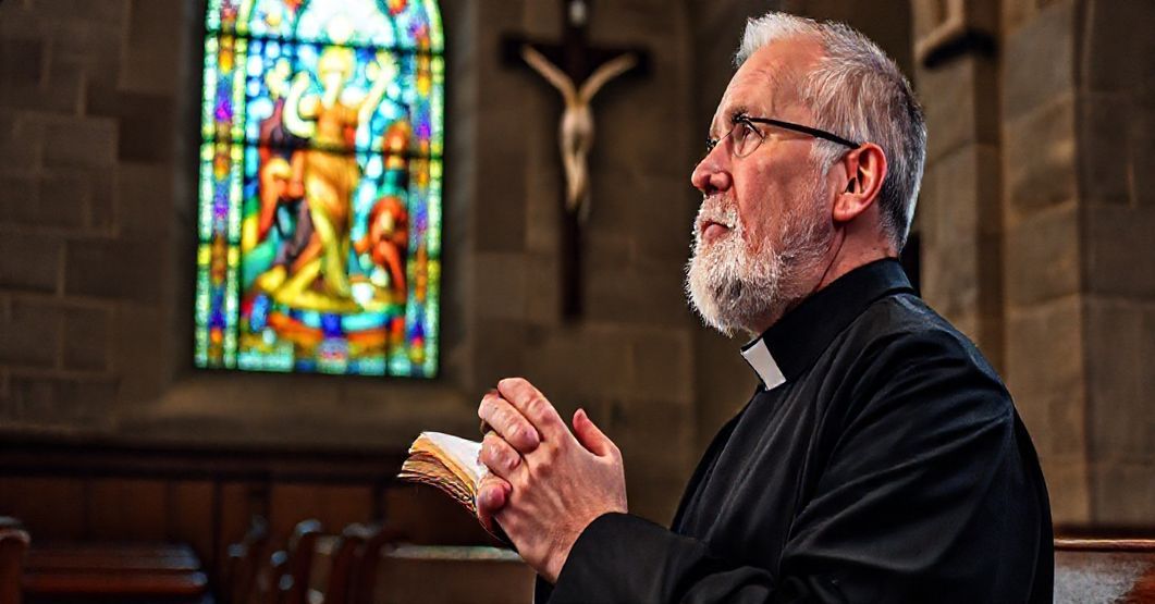 Kapelan modli się przed krzyżem z książką Petera Seewalda "Odkrycie wieczności" w tradycyjnym kościele katolickim