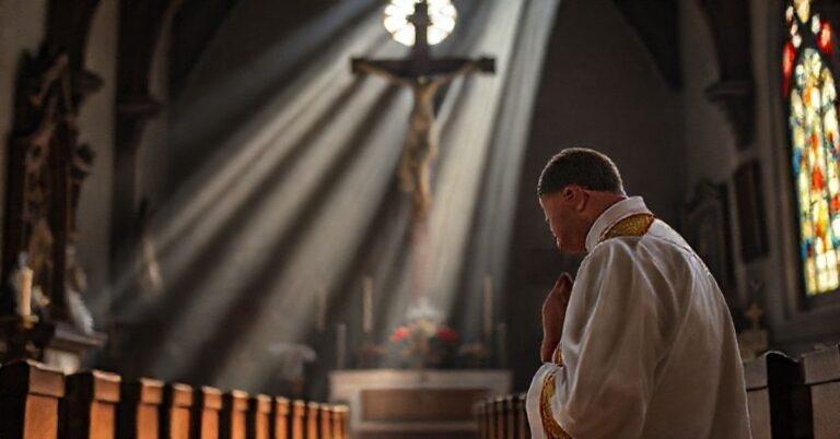 Sobieszcza postać kapłana w tradycyjnych szatach liturgicznych modlącego się przed krzyżem w tradycyjnym kościele