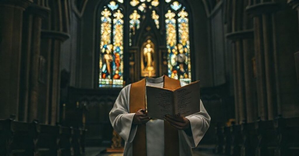 Sobótni kapłan w tradycyjnych szatach stoi w ciemnym kościele przed ołtarzem z książką Alberta Cohena.