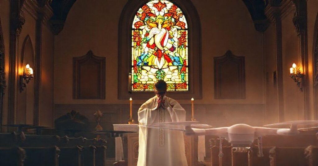 Kaplica katolicka z kapłanem modlącym się przy ołtarzu, z witrażem przedstawiającym Serce Jezusa w tle.