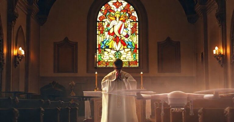 Kaplica katolicka z kapłanem modlącym się przy ołtarzu, z witrażem przedstawiającym Serce Jezusa w tle.