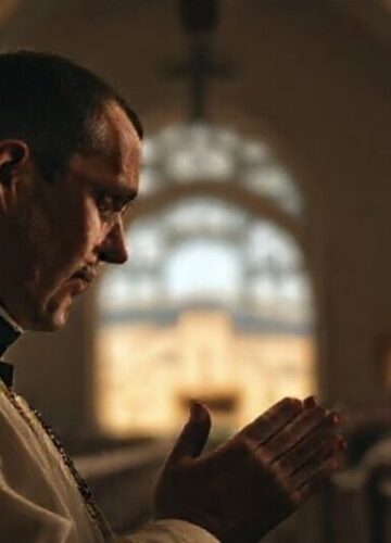 Modlitwa za pokój w Ziemi Świętej - katolickie perspektywy Prawy katolicki kapłan modli się w koście z widokiem Ziemi Świętej na tle, symbolizując duchowy wymiar konfliktu izraelsko-palestyńskiego.