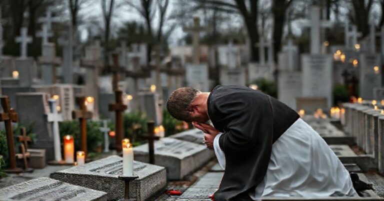 Kneeling Catholic priest at war memorial in Warsaw, honoring Polish martyrs with traditional Catholic reverence.