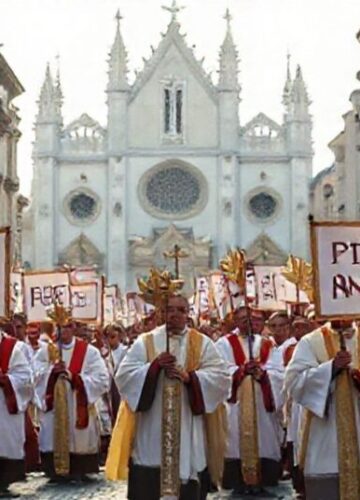 Katolicki pochód w obronie życia i rodziny Pochód katolicki w tradycyjnych szatach liturgicznych z transparentami 'Ochrona Życia i Rodziny' na tle gotyckiego kościoła.