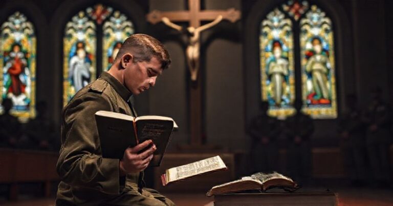 Stojący żołnierz w katolickim stroju wojskowym modli się przed krucyfiksem, trzymając zakazane książki o ideologii gender i "1984" Orwella