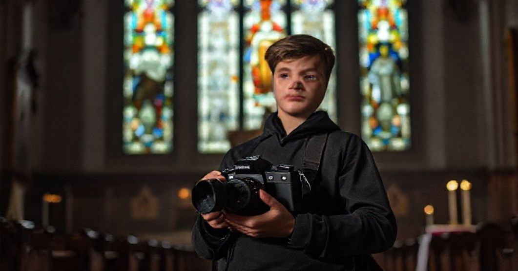 Młody katolicki uczeń z aparatem fotograficznym w kościele, rozmyślający nad konfliktem między sztuką świecką a sakralną