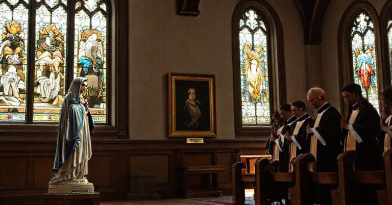 Wnętrze tradycyjnego kościoła katolickiego z witrażami przedstawiającymi sceny biblijne. Wśród nich umieszczono portret admirała Richarda Levine'a z poprawioną tabliczką z imieniem urodzenia oraz grupą duchowieństwa modlącego się.