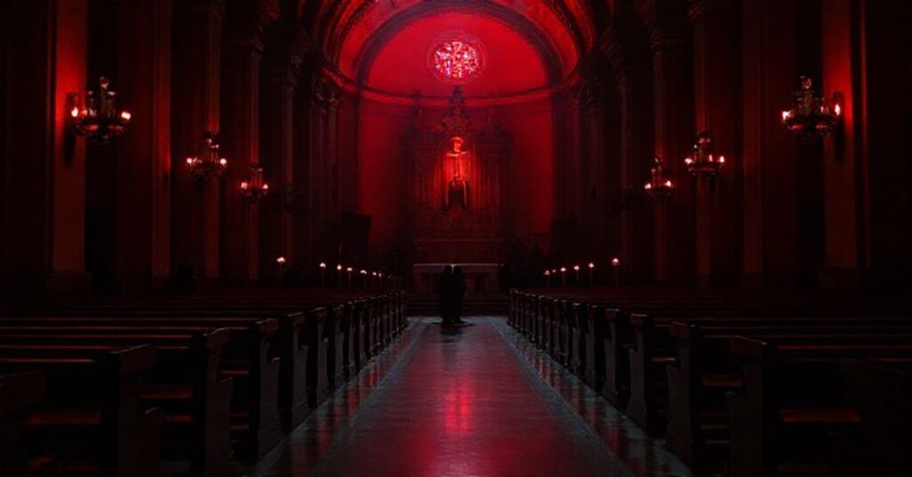 Ciemny wnętrze kościoła Św. Bartłomieja na Wyspie w Rzymie oświetlone czerwonym światłem podczas kampanii 'Red Week', symbolizujące duchową pustkę współczesnego ekumenizmu.