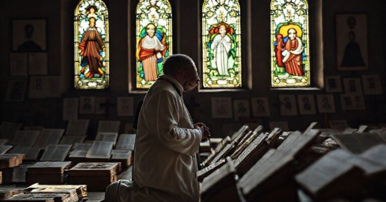 Ksiądz w tradycyjnych szatach liturgicznych modli się przed pomnikiem w obozie koncentracyjnym Majdanek