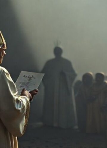 Krytyka humanitaryzmu zastępującego wiarę Ksiądz w tradycyjnym ornacie stojący przed grupą biednych ludzi otrzymujących pomoc materialną; w tle widnieje cień osoby symbolizującej fałszywego papieża. Scena podkreśla brak duchowego wsparcia i nadmierne skupienie na pomocy materialnej.