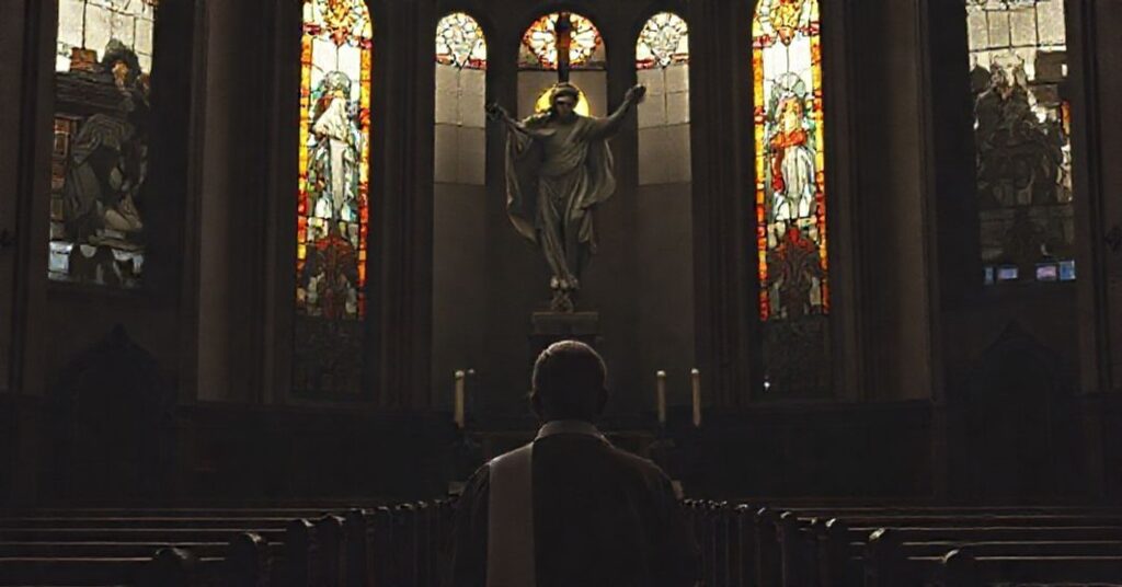 Wnętrze tradycyjnego kościoła katolickiego w Hiszpanii z księdzem modliącym się przed posągiem Chrystusa Króla.