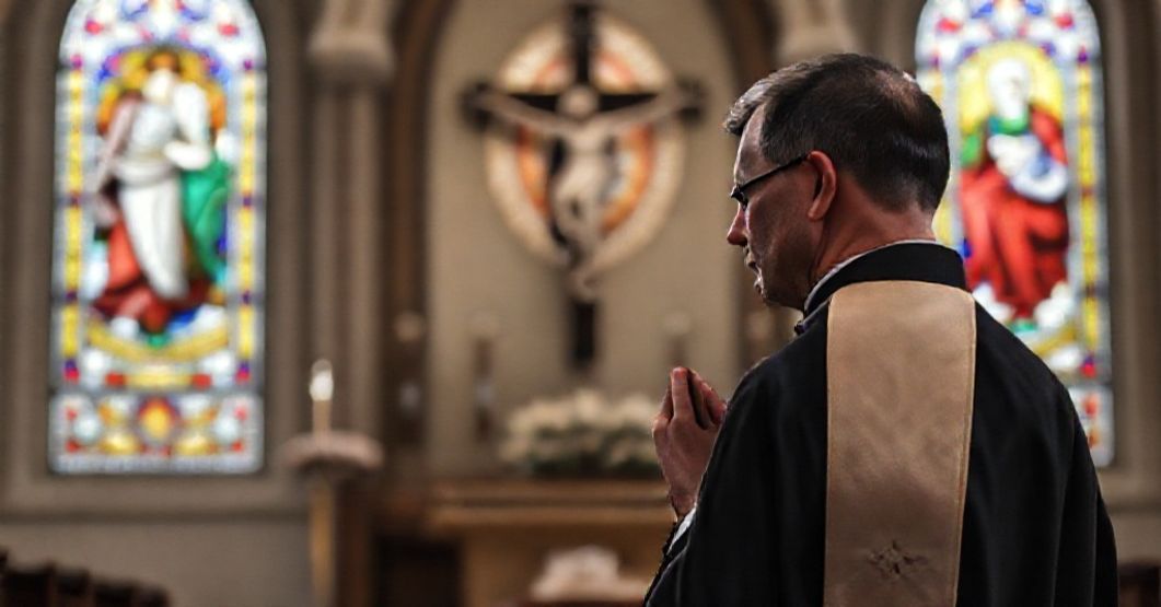Tradycyjny ksiądz w sutannie modli się przed krzyżem w kościele z oknami witrażowymi przedstawiającymi Serce Pana Jezusa i Matkę Boską Bolesną. Scena wyraża głęboką pobożność i duchową tęsknotę.