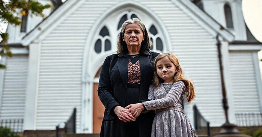 Matka katolicka trzymająca ręce swojej córki przed kościołem w Maine, symbolizując walkę z tyranią sądową.