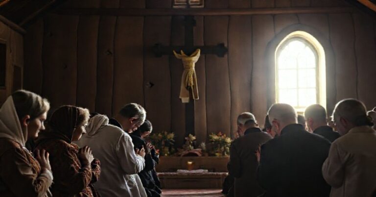 Grupa wiernych modli się przed pomnikiem poświęconym męczennikom wołyńskim w prostej kaplicy drewnianej.
