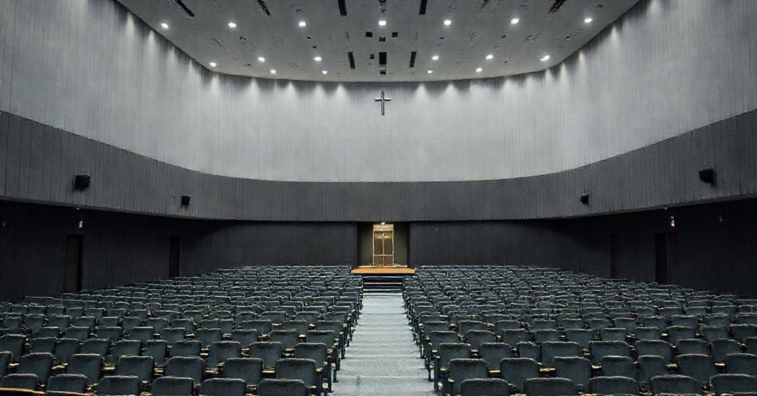 Obraz przedstawiający nowoczesne seminarium w Tarnowie z modernistyczną architekturą. W centrum uwagi znajduje się duża sala konferencyjna przeznaczona do wydarzeń świeckich, a w tle mała, prawie ukryta kaplica. Scena jest pozbawiona katolickich symboli, podkreślając brak formacji doktrynalnej. Atmosfera wydaje się być bardziej biurokratyczna niż duchowa.