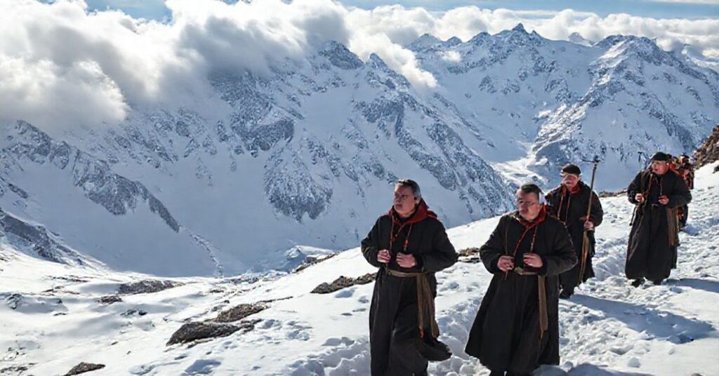 Grupa pielgrzymów w tradycyjnych katolickich ubraniach poruszająca się po zasłożenym śniegiem w Tatrach. Scena podkreśla duchową refleksję i zależnłość od Bożej OpatrznoŜi w obliczu przyrodniczych wyzwań.