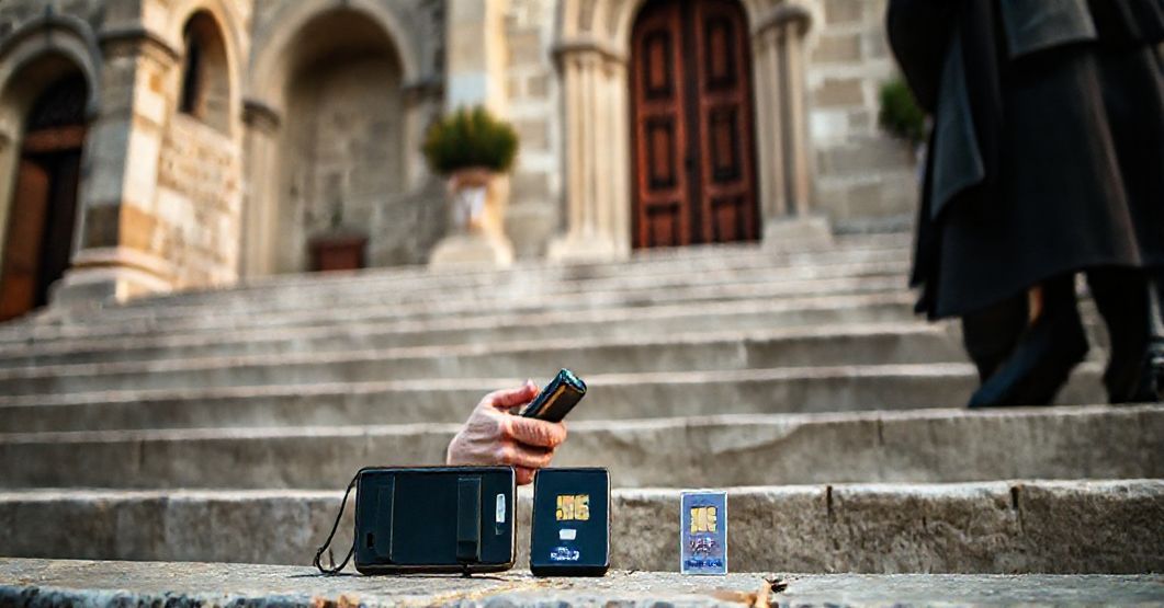 Katolicki pielgrzym modli się przed europejskim kościołem z różańcem w ręku, z nieużywanym telefonem i kartą eSIM na schodach.