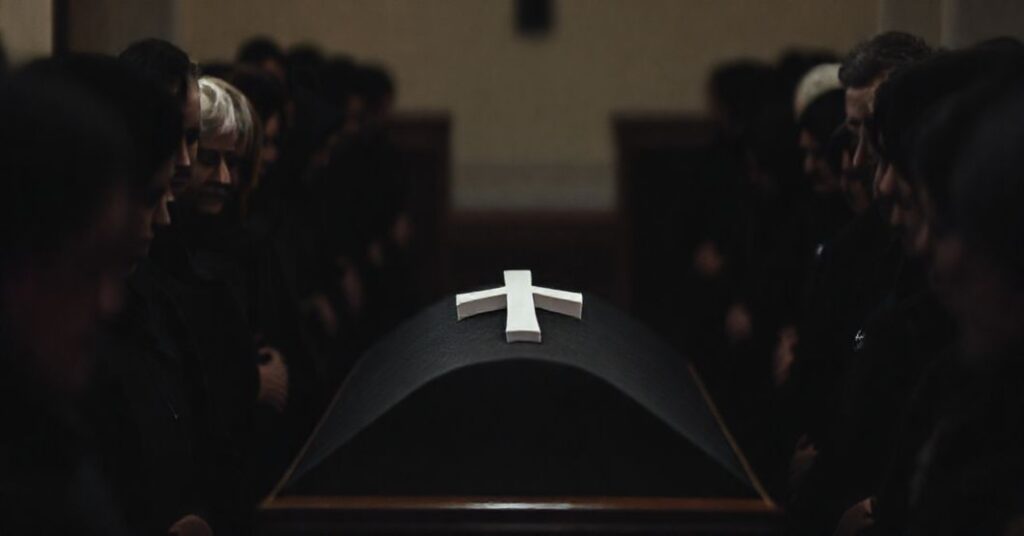 Scena pogrzebowa katolicka bez modlitw i obrzędów, z trumną i krzyżem, w XIX-wiecznym stylu tradycyjnym.