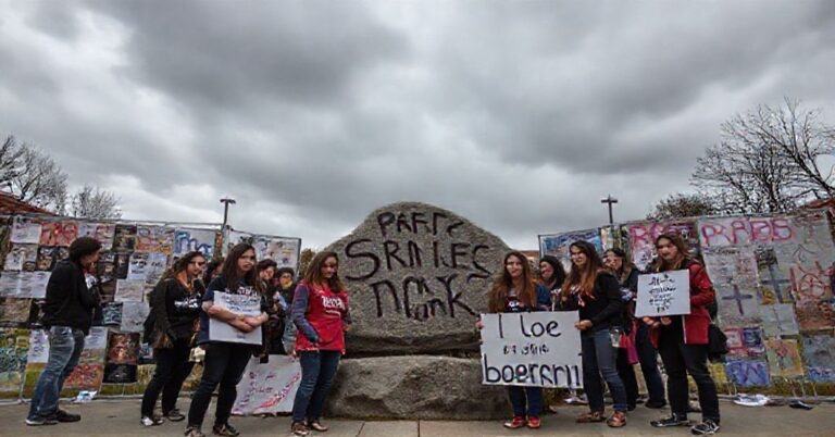 Grupa "Students for Life" na Uniwersytecie w Mary Washington stoi przed sprzeniewierconymi plakatami i deflowanym kamieniem "Spirit Rock" podczas protestu z powodu aborcji. Scena jest poważna i symboliczna.