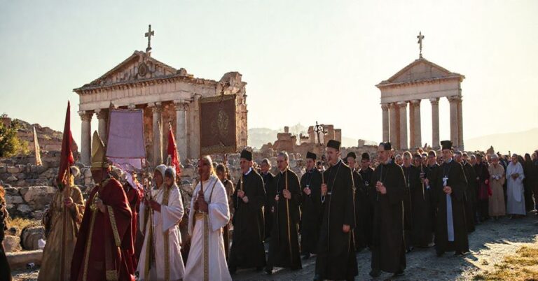 Procesja katolicka w Turcji z wiernymi trzymającymi sztandary i świece przed ruinami chrześcijańskimi w tle ekumenicznego zgromadzenia.