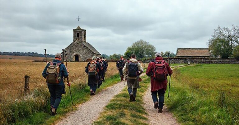 Grupa pielgrzymów idąca szlakiem Via Francigena przez angielską wieś, mijając stary kościół.