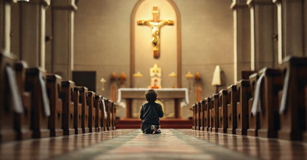 Zdjęcie przedstawiające dziecko modlące się w tradycyjnym kościele katolickim z krzyżem na tle, symbolizujące pustkę religijności w humanistycznych narratywach.