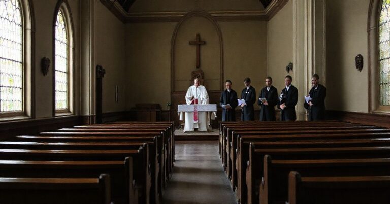 Pusty wnętrze tradycyjnego kościoła z pustymi ławkami i opustoszałym ołtarzem na pierwszym planie. W tle spotykają się współczesni klerycy w salonie konferencyjnym z mikrofonami.
