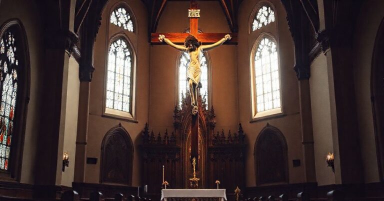 Stary drewniany krzyż wiszący nad ołtarzem w tradycyjnym kościele katolickim, symbolizujący pasję i zmartwychwstanie Chrystusa.