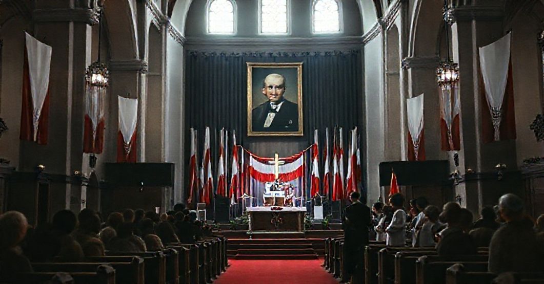 Wnętrze kościoła, gdzie scena koncertowa zastępuje ołtarz, z widocznymi elementami patriotycznymi i portretem Stanisława Soyki. Modernistyczni duchowni stoi blisko sceny.